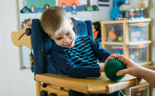 a child with diverse abilities playing with touchy spiked green ball with a caregiverr's assistance