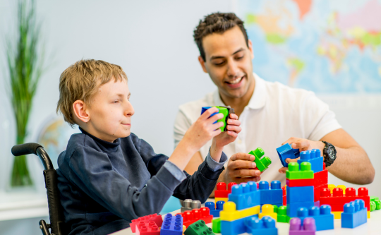 a child with diverse abilities playing with large lego blocks with a caregiver 