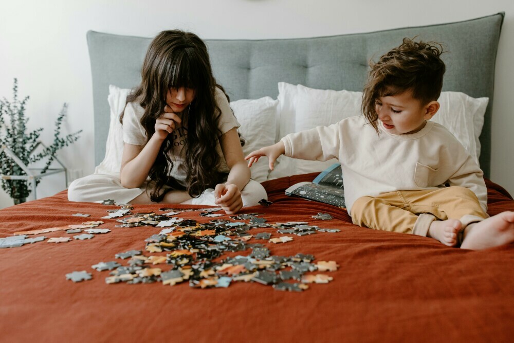 two children playing on the bed with different color puzzles and putting them together